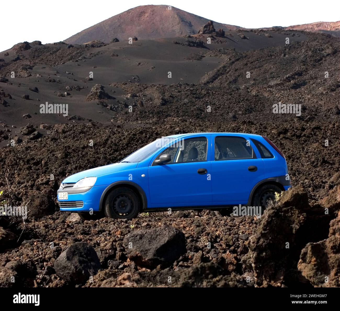 Un'auto blu a noleggio circondata da rocce vulcaniche e montagne presso il monumento naturale Los Volcanes de Teneguía, la Palma, Isole Canarie, Spagna Foto Stock