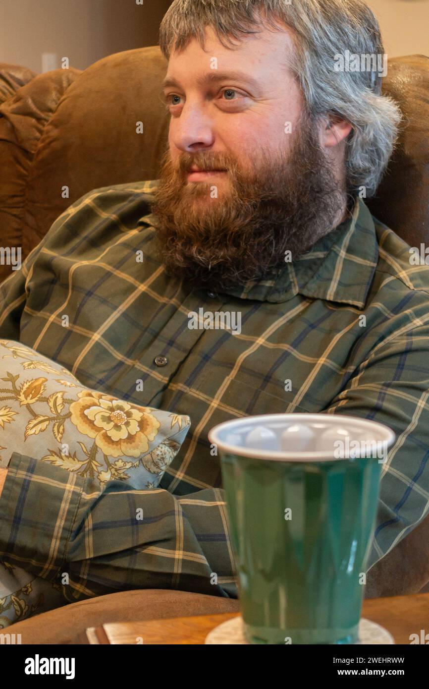 uomo caucasico adulto di 35 anni con baffi e barba marrone riccia che diventa prematuramente grigio sulla testa. Primo piano, sorridendo. Foto Stock