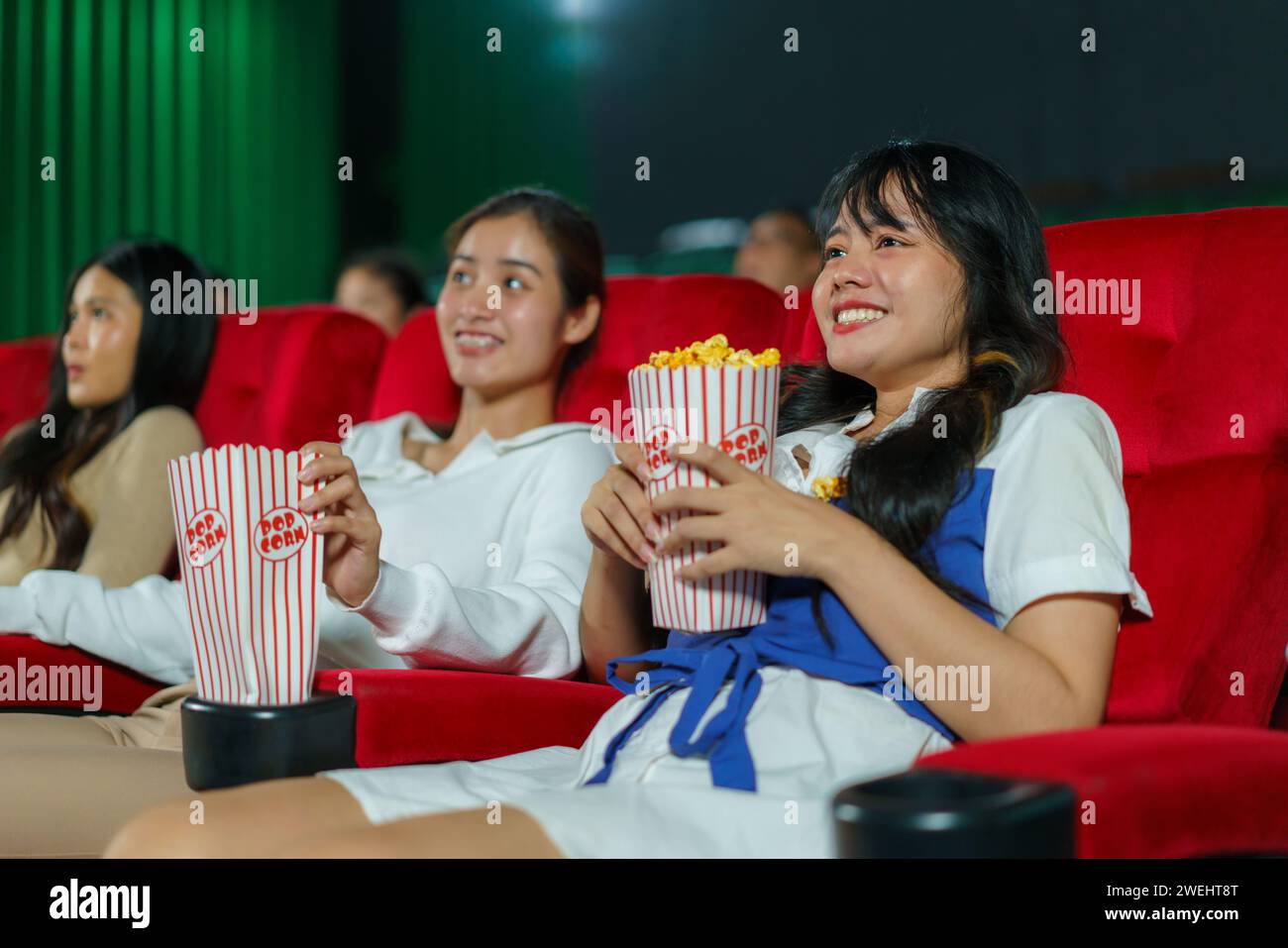Un gruppo di donne guarda con piacere un film, ognuna con in mano una busta di popcorn Foto Stock