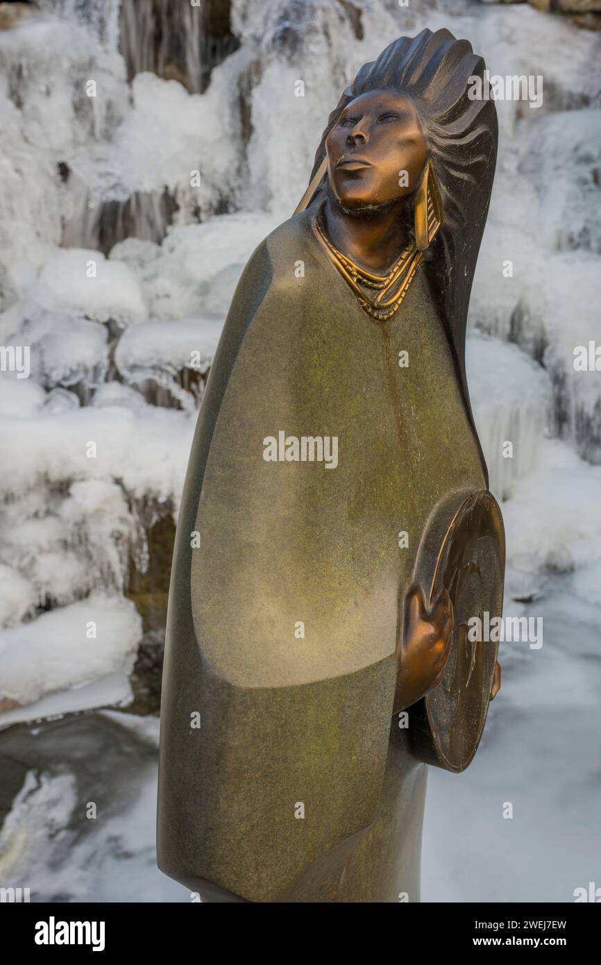 Una statua di bronzo in inverno che si trova in una fontana d'acqua ghiacciata nel giardino dei condomini Shumway a Kirkland, nello stato di Washington, USA. Foto Stock