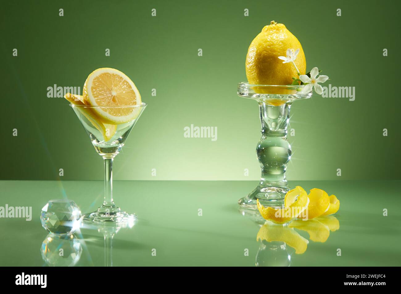 Concetto di lusso per pubblicizzare prodotti a base di ingredienti di limone. Fette e scorza di limone decorate su sfondo verde con una tazza di vetro di cristallo. Copia Foto Stock