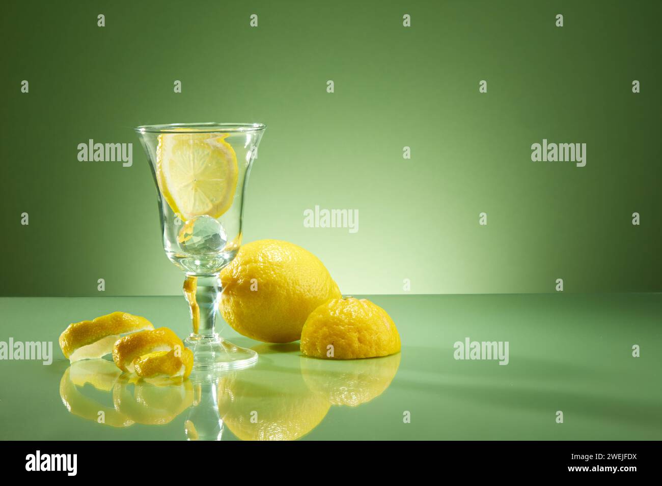 Vista frontale della tazza di vetro contenente fette di limone, limone e buccia decorata su sfondo verde retroilluminato. Spazio vuoto per testo e design. ph. Pubblicitario Foto Stock