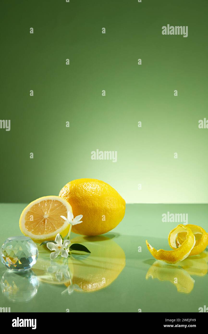 Vista frontale della buccia e delle metà di limone, fiore bianco e palla di cristallo decorate su sfondo verde. Scena minima con spazio vuoto per mostrare le tue pr Foto Stock