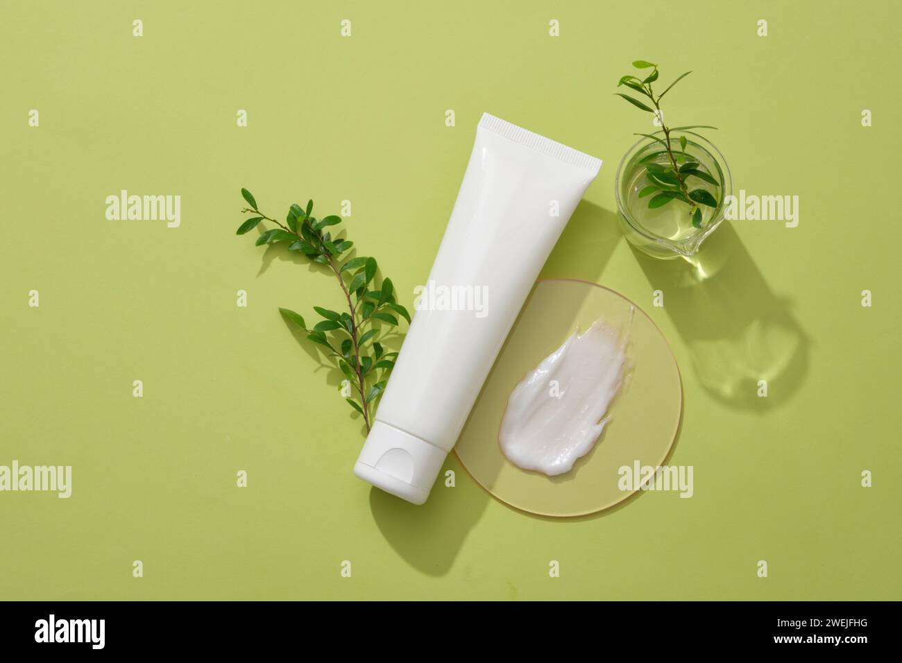 Composizione di foglie verdi, flacone cosmetico senza etichetta e consistenza crema su podio decorato su sfondo verde. Scena minimalista per il cosmo pubblicitario Foto Stock