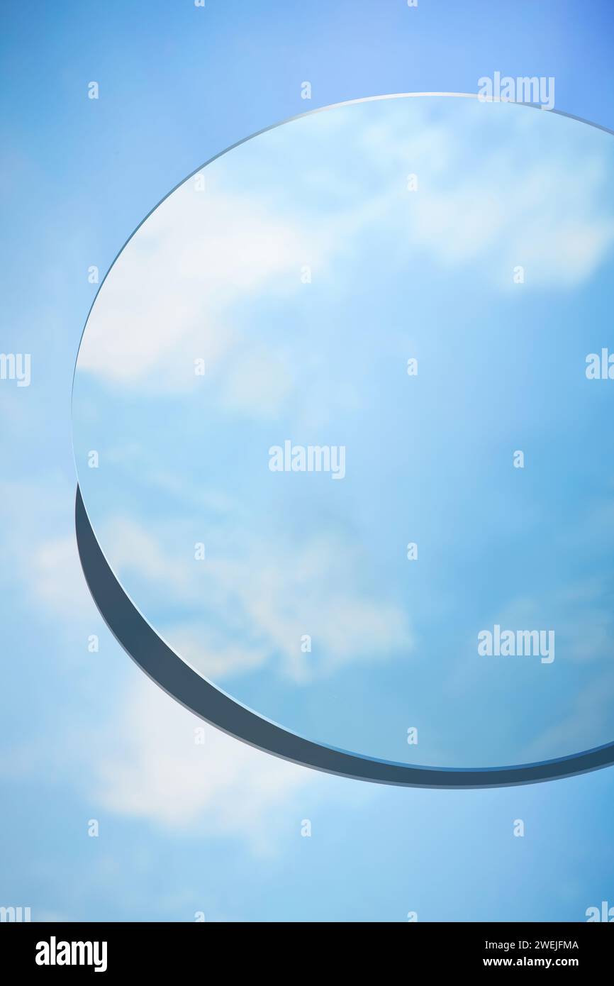 Scenografia minimale astratta con specchio rotondo posizionato su sfondo blu. Lo specchio riflette il cielo azzurro e le nuvole bianche. Copia spazio Foto Stock