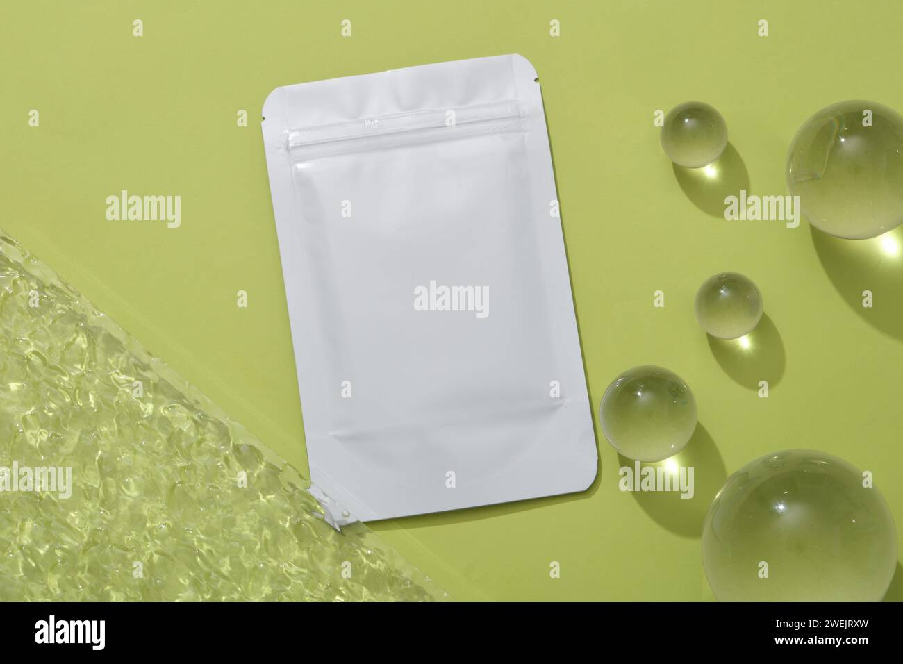 Mockup di un pacchetto di maschere facciali decorate con alcune palle di vetro e foglio acrilico su sfondo verde. Spazio per il design. Scena minimalista per il marchio Foto Stock