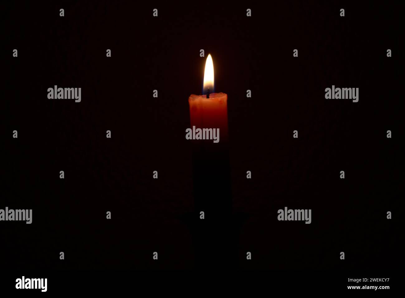 Su uno sfondo nero testurizzato una candela rossa accesa, messa a fuoco morbida Foto Stock