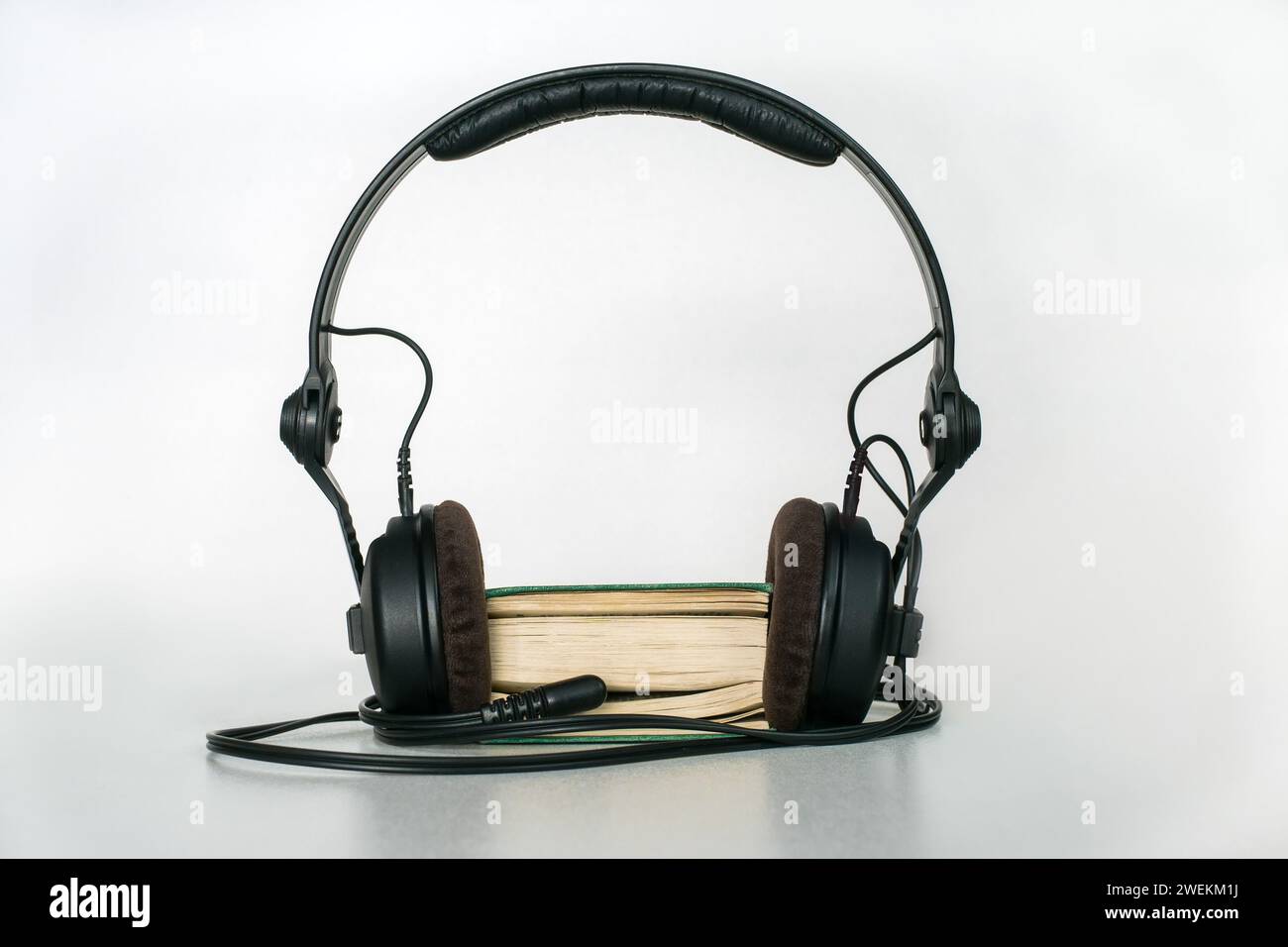 Un libro tascabile con cuffie e una spina mini-jack inserita tra le pagine su sfondo chiaro. Concetto di audiolibro Foto Stock