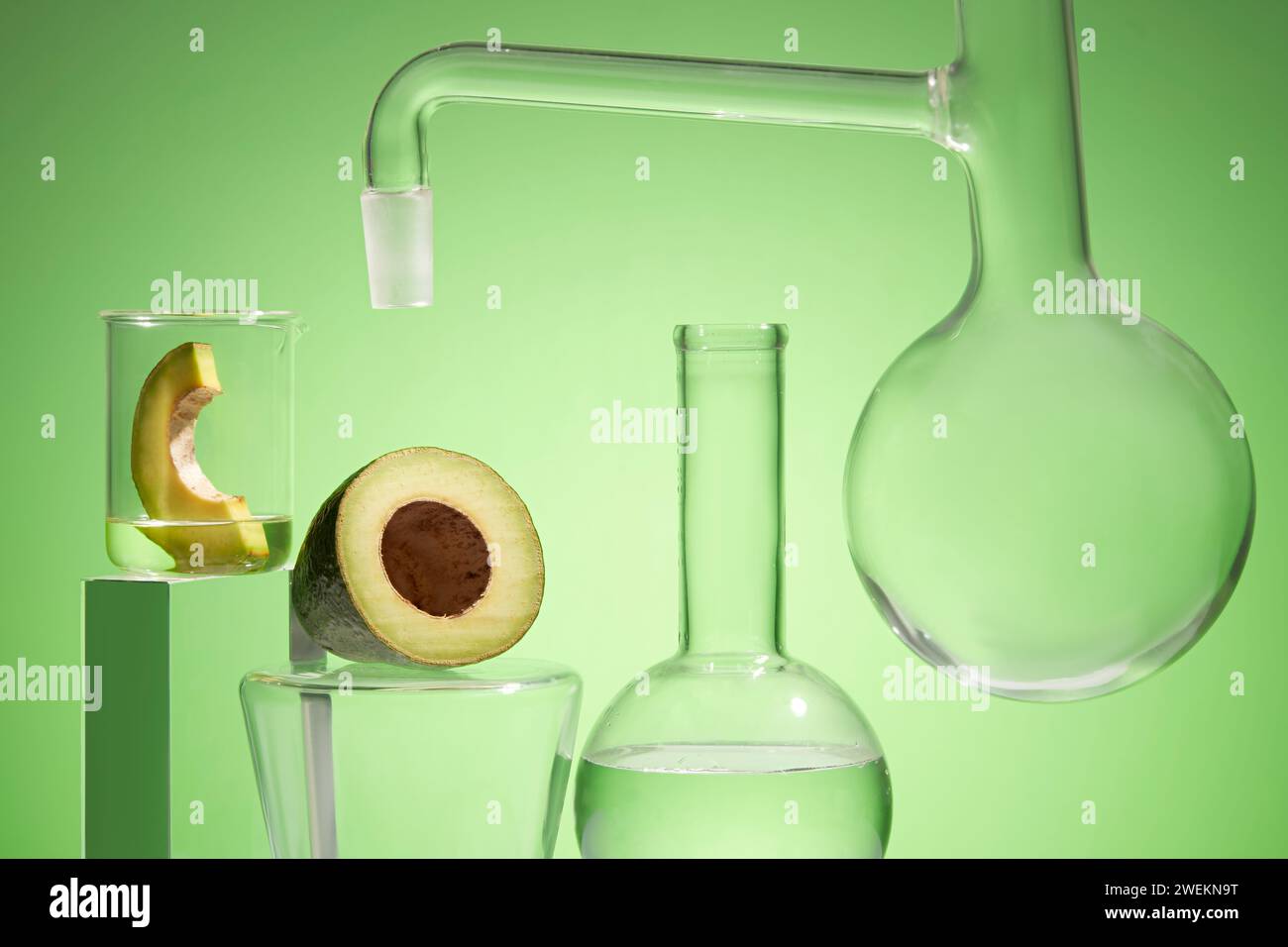 Scenario di ricerca di prodotti cosmetici con estratto di avocado in laboratorio con vetreria da laboratorio e fette di avocado biologico fresche decorate sul dorso verde Foto Stock