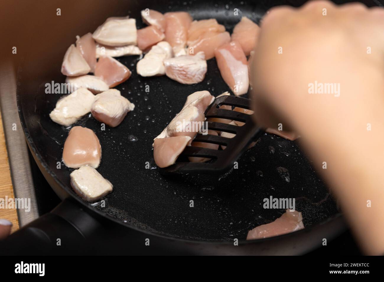 Baviera, Germania - 25 gennaio 2024: Donna che frigge strisce di pollo in una padella calda con olio sulla stufa *** Frau brät beim Kochen Hähnchenfleisch Streifen in einer heißen Pfanne mit Öl auf dem Herd an Foto Stock