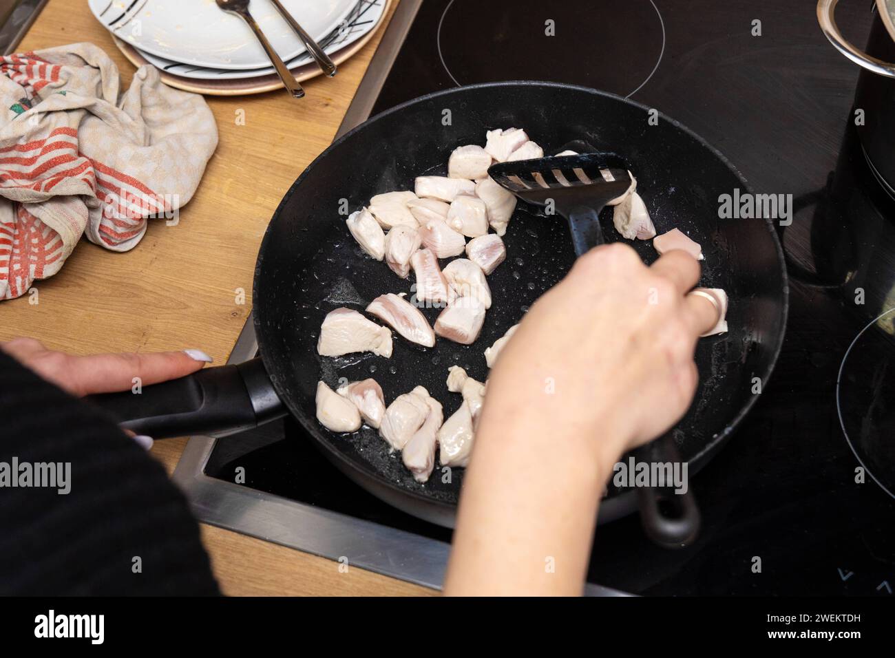 Baviera, Germania - 25 gennaio 2024: Donna che frigge strisce di pollo in una padella calda con olio sulla stufa *** Frau brät beim Kochen Hähnchenfleisch Streifen in einer heißen Pfanne mit Öl auf dem Herd an Foto Stock