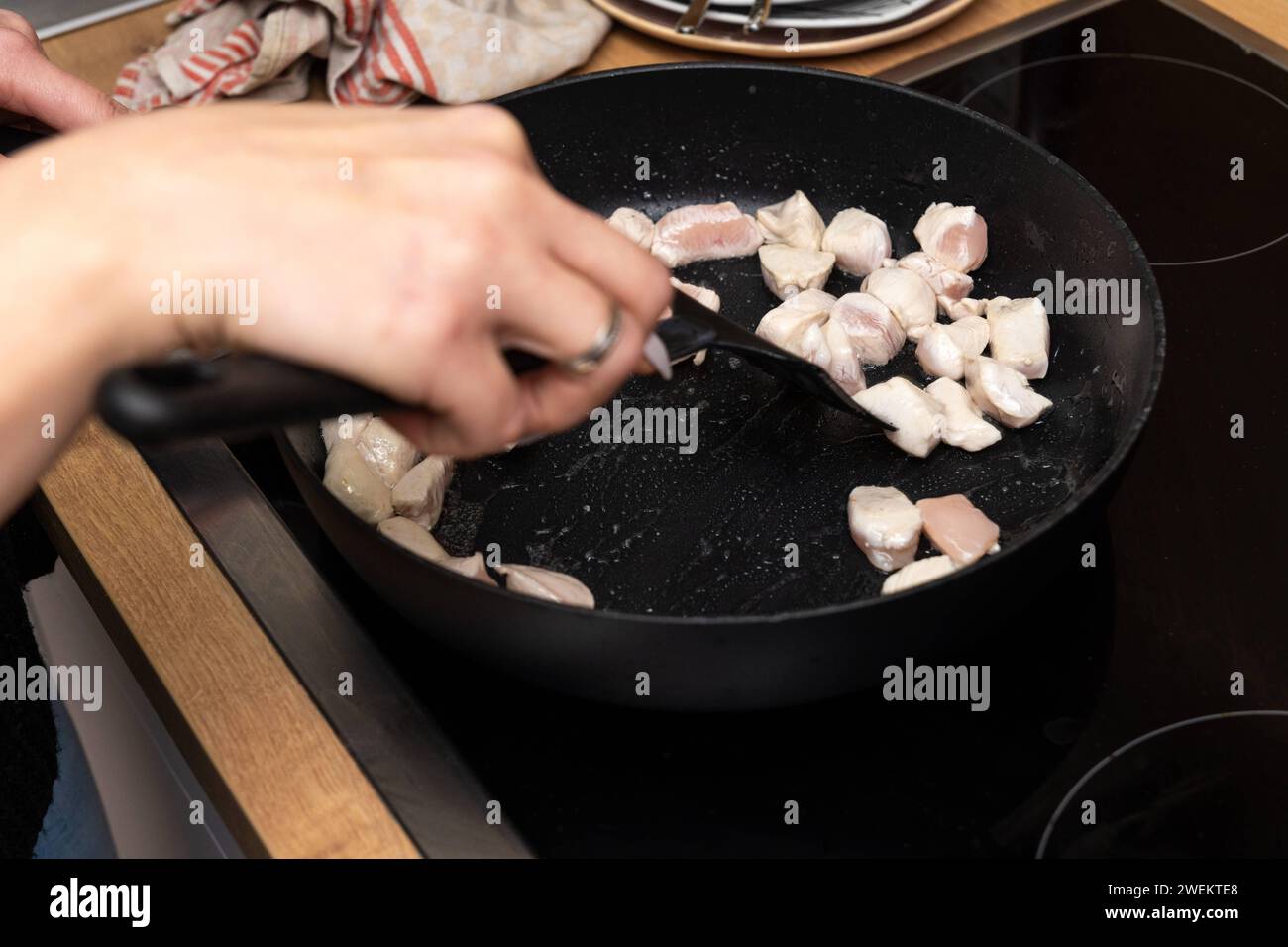 Baviera, Germania - 25 gennaio 2024: Donna che frigge strisce di pollo in una padella calda con olio sulla stufa *** Frau brät beim Kochen Hähnchenfleisch Streifen in einer heißen Pfanne mit Öl auf dem Herd an Foto Stock