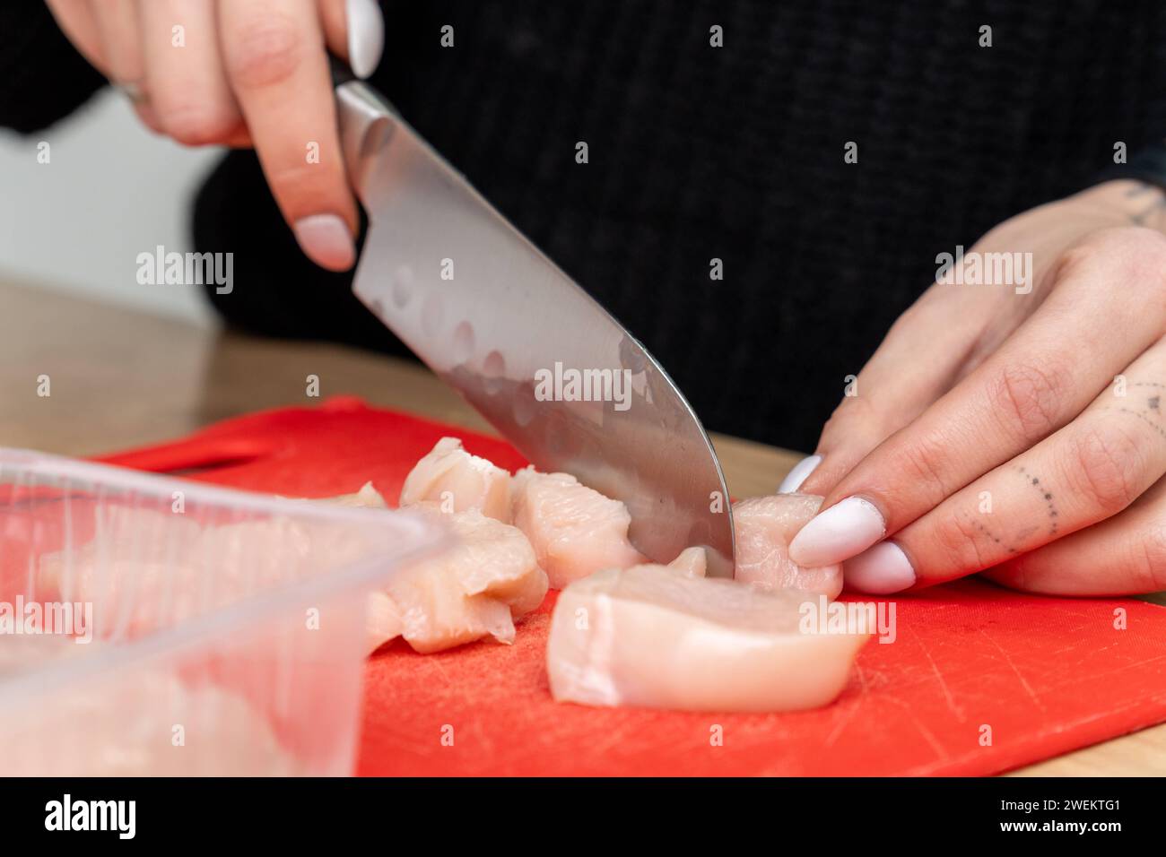 Baviera, Germania - 25 gennaio 2024: Donna che trita carne di pollo in una cucina sul piano di lavoro con un tagliere e un coltello affilato. Giovane donna che cucina *** Frau schneidet in einer Küche auf der Arbeitsplatte mit einem Schneidebrett und scharfem Messer Hähnchenfleisch klein. Junge Frau beim Kochen Foto Stock