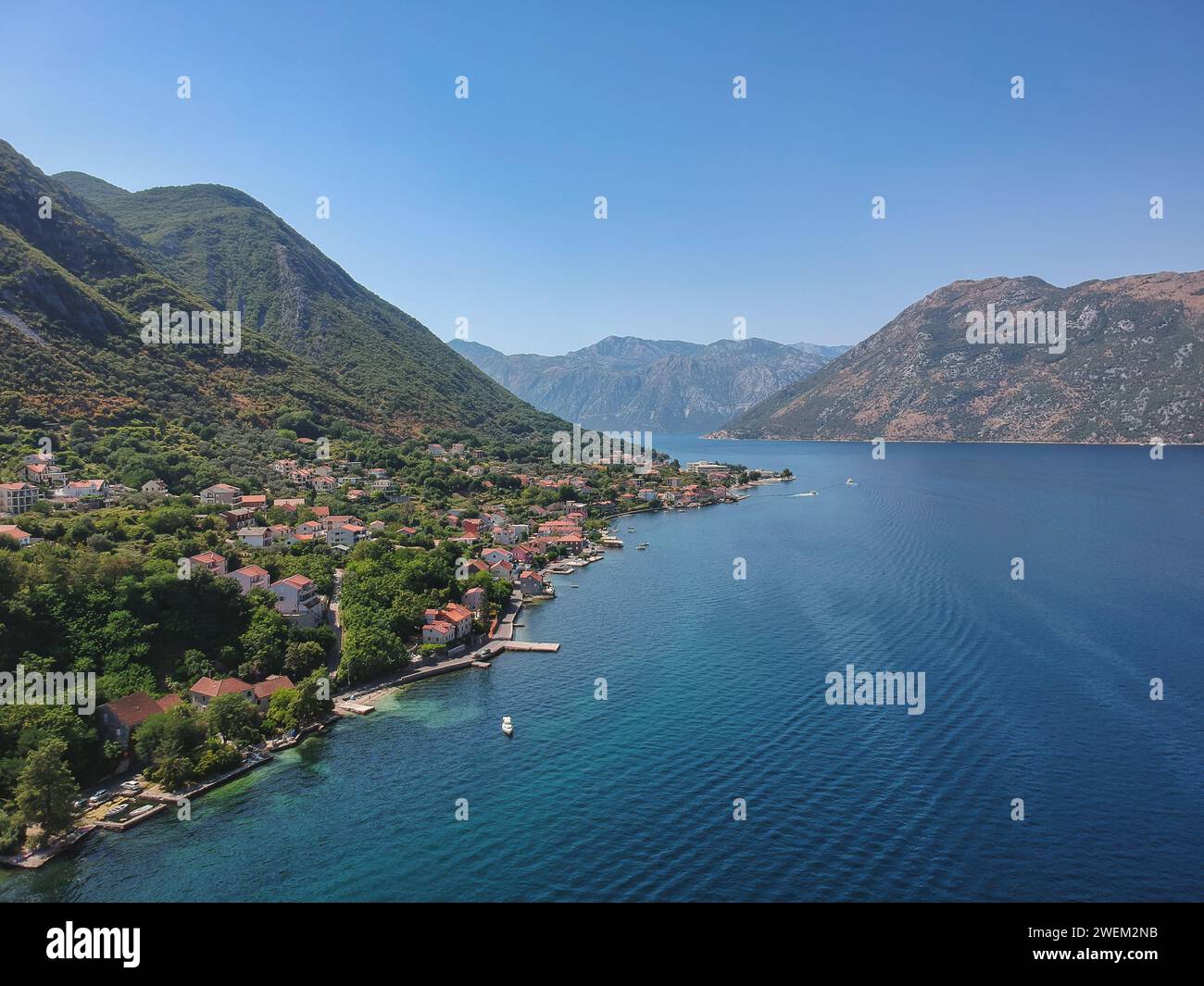 Vista dall'alto di un incantevole villaggio di Prcanj lungo le acque azzurre della baia di Cattaro, circondata dalle lussureggianti montagne del Montenegro. Foto Stock