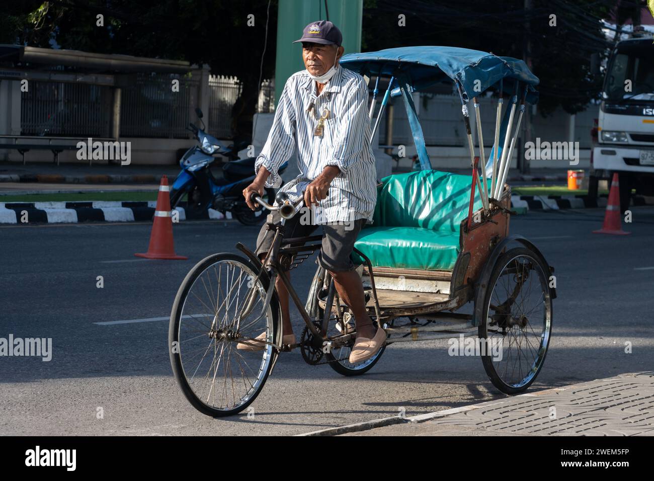 SAMUT PRAKAN, THAILANDIA, 12 novembre 2023, Un uomo guida un triciclo per trasportare un passeggero in una strada cittadina Foto Stock
