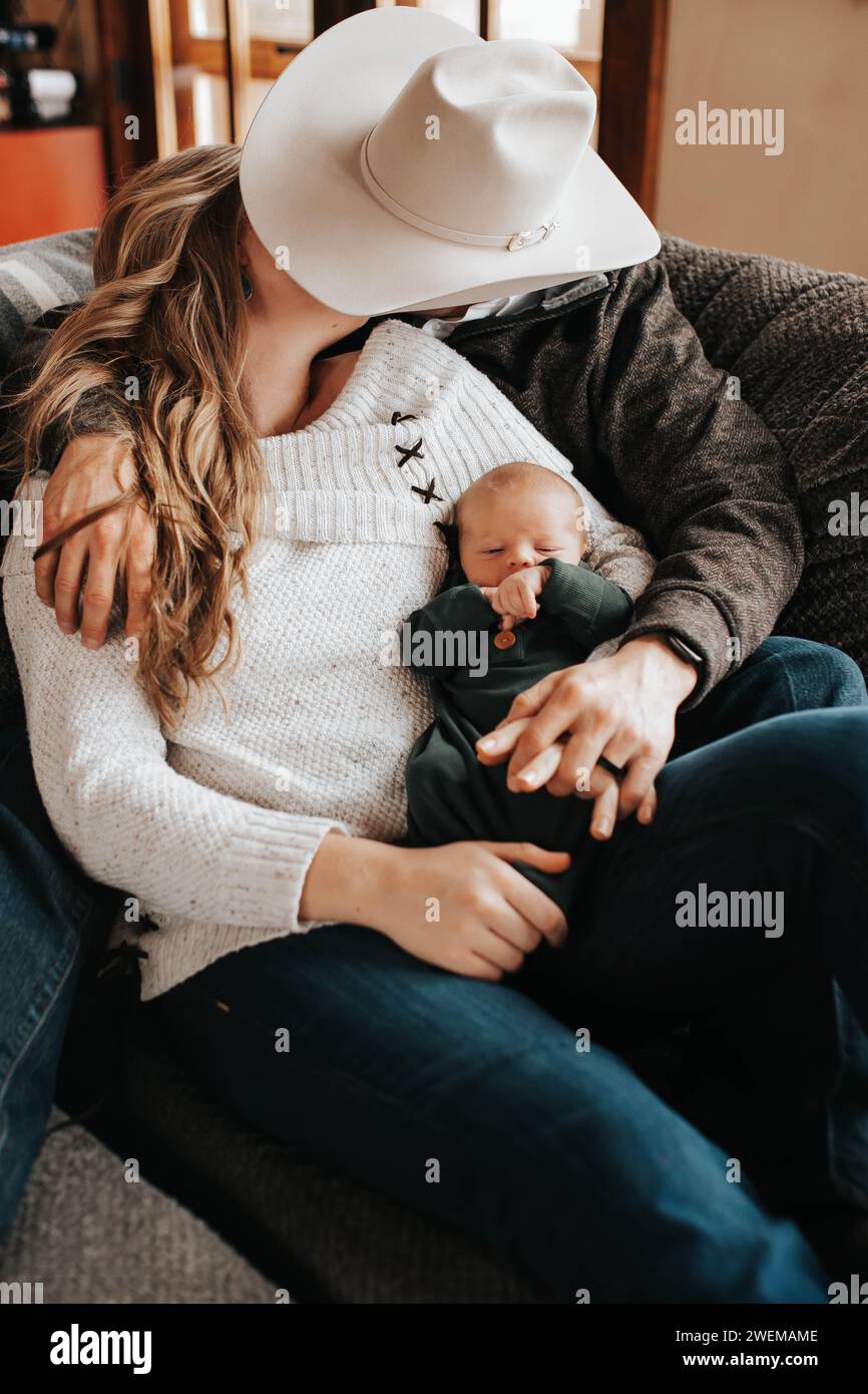 Il neonato si coccola con i genitori sul divano, baciandosi Foto Stock