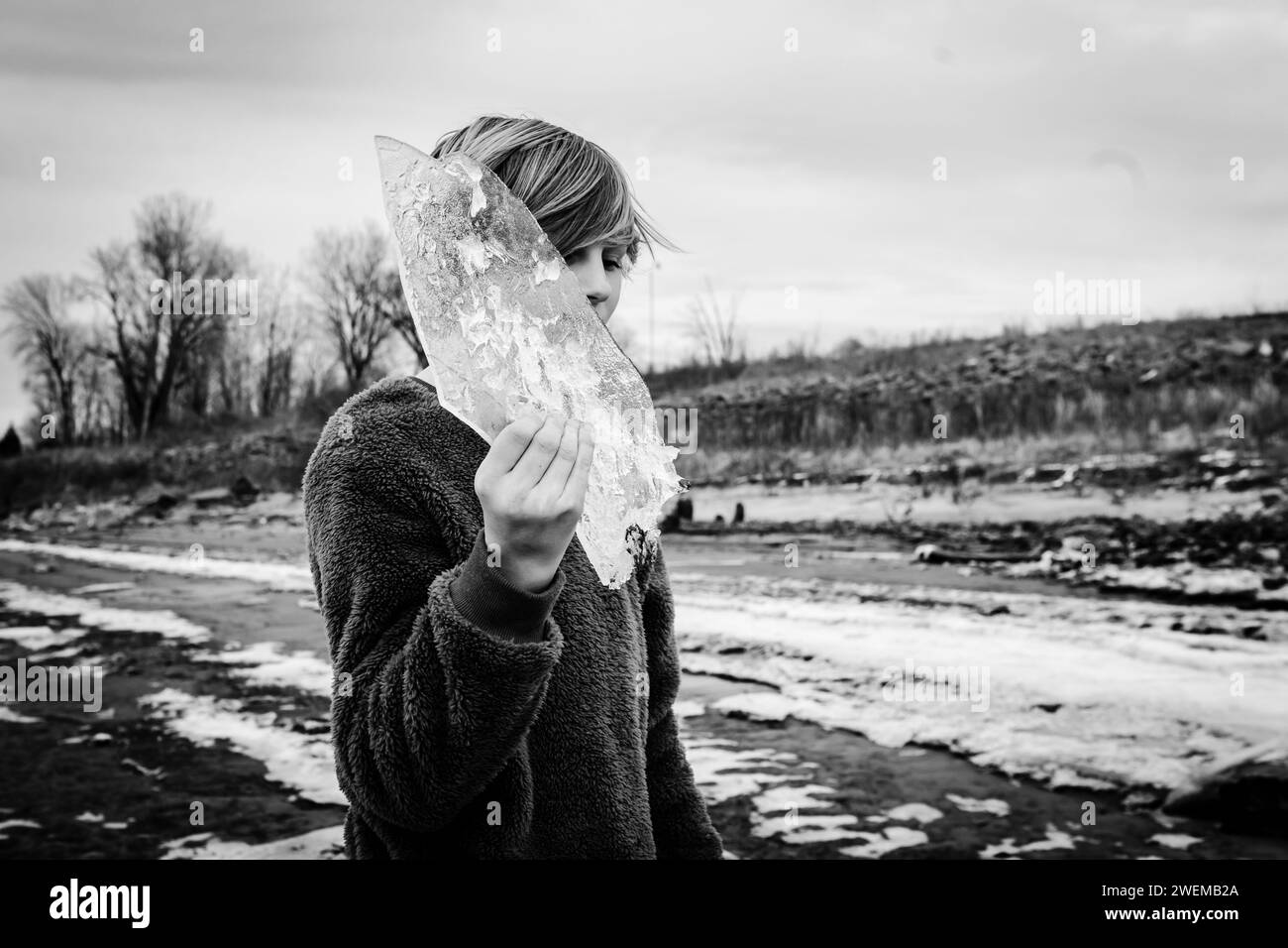 Ragazzo pre-adolescente che esplora la riva del fiume con un foglio di ghiaccio congelato Foto Stock