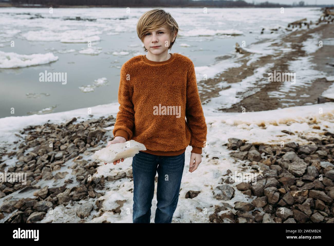 Ragazzo pre-adolescente sulla riva ghiacciata che tiene un pezzo di ghiaccio Foto Stock