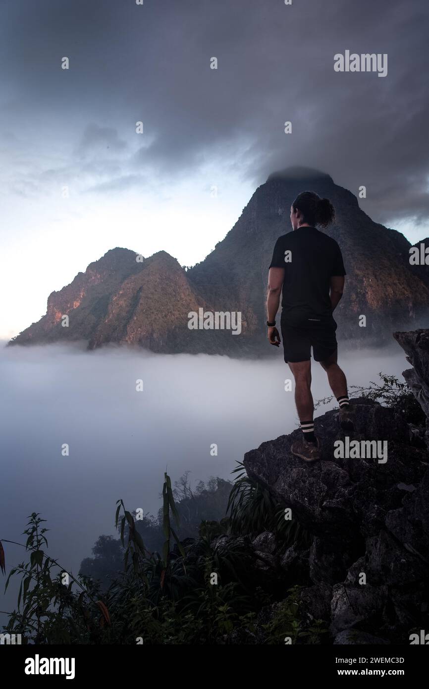 Escursionista maschile che indossa un vestito nero, ammirando la vista durante l'alba Foto Stock