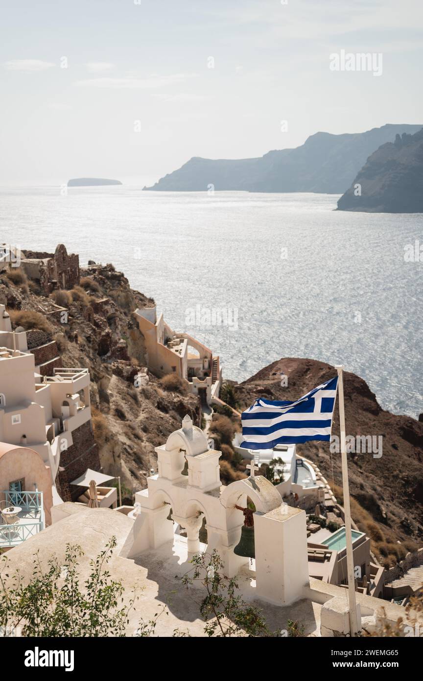 Bandiera greca e campane della chiesa che si affacciano sul villaggio di Oia Foto Stock