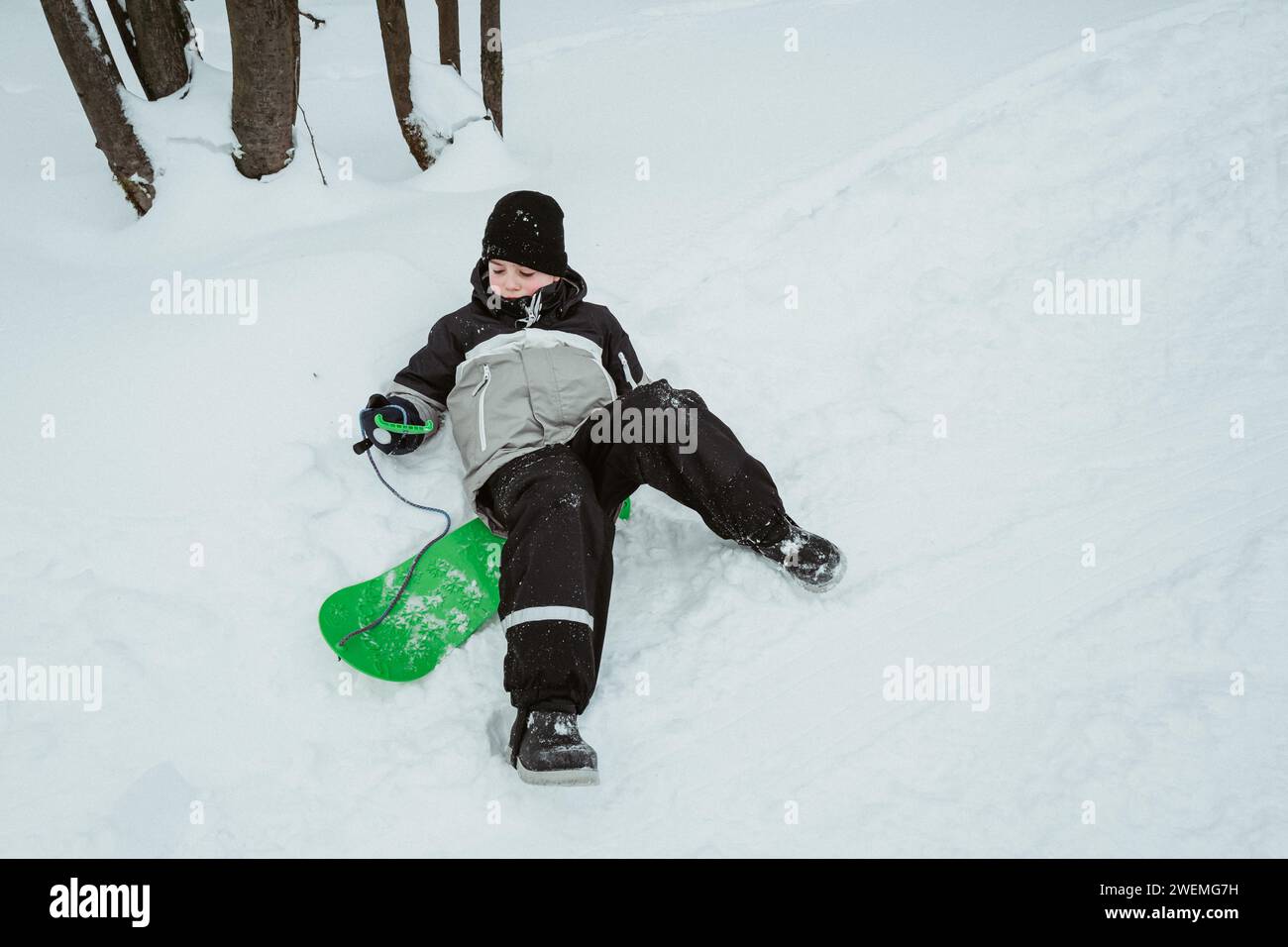 Un ragazzo fa snowboard in una foresta innevata invernale e cade Foto Stock
