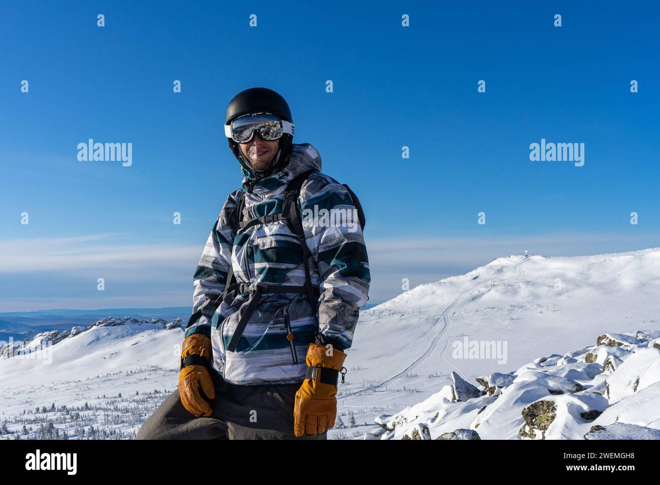 Uomo soddisfatto alla stazione sciistica di Sheregesh, sullo sfondo delle piste innevate di montagna nelle giornate di sole. Attività invernali. Uomini in attrezzatura da snowboard BL Foto Stock