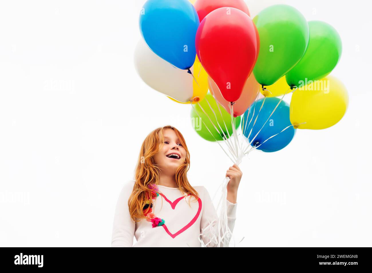 Felice bambina di 8-9 anni con i capelli rossi che regge palloncini colorati all'elio Foto Stock