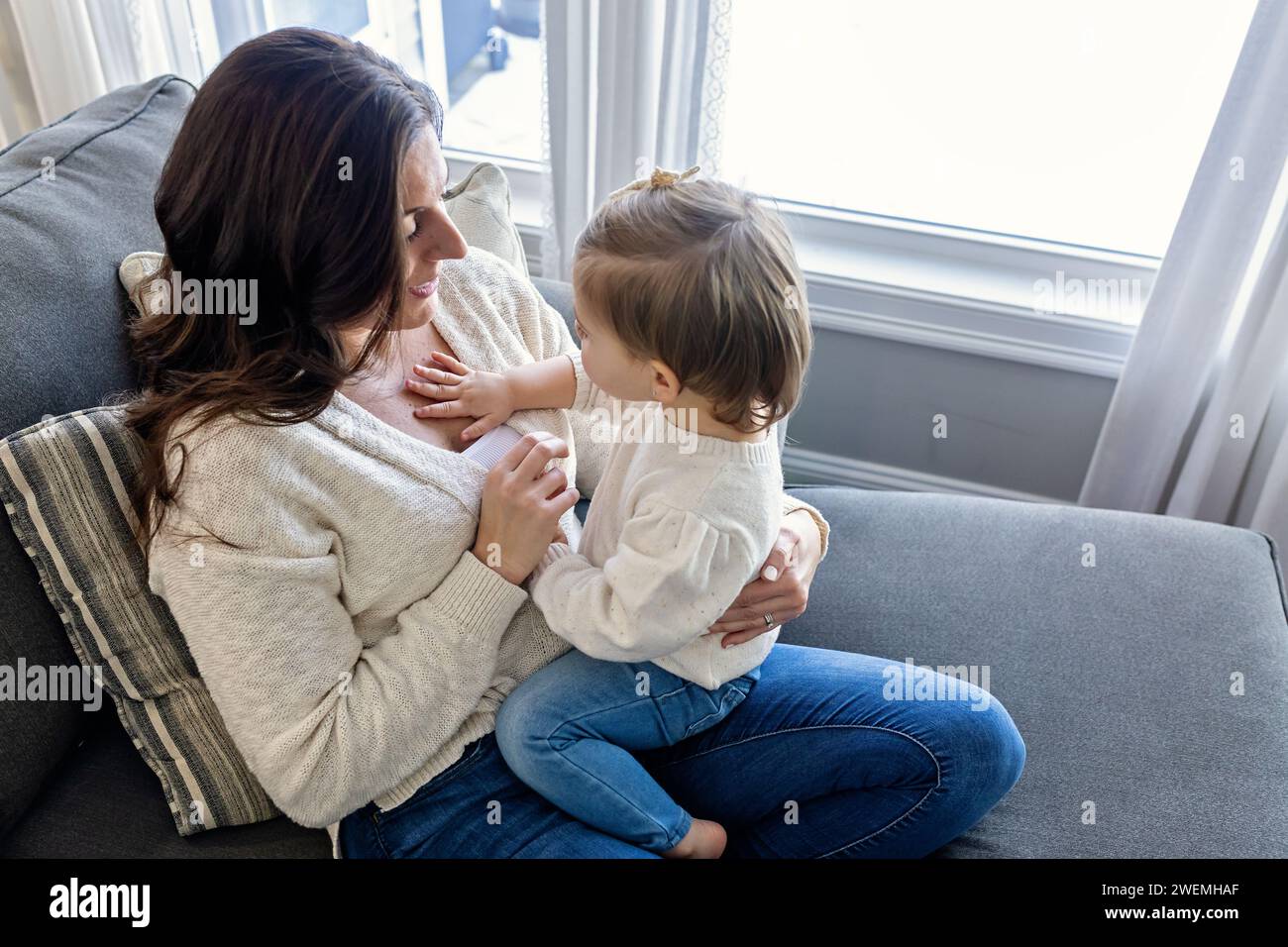 Bambina seduta sul Lap Cuddling della mamma Foto Stock