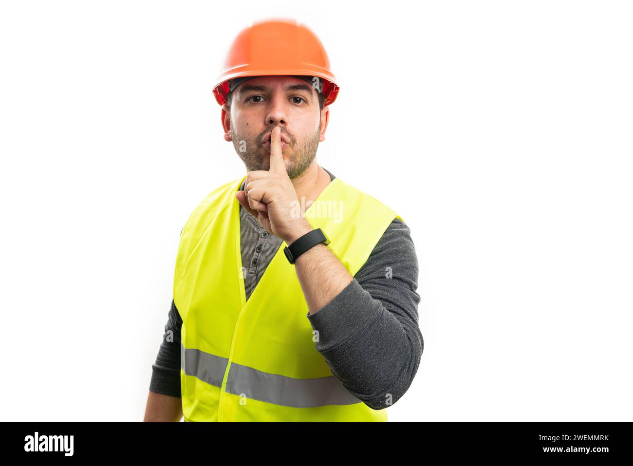 Adulto costruttore uomo in abbigliamento da lavoro casco di sicurezza gilet fluorescente che fa shush gesture con indice dito sopra la bocca come concetto segreto isolato su wh Foto Stock