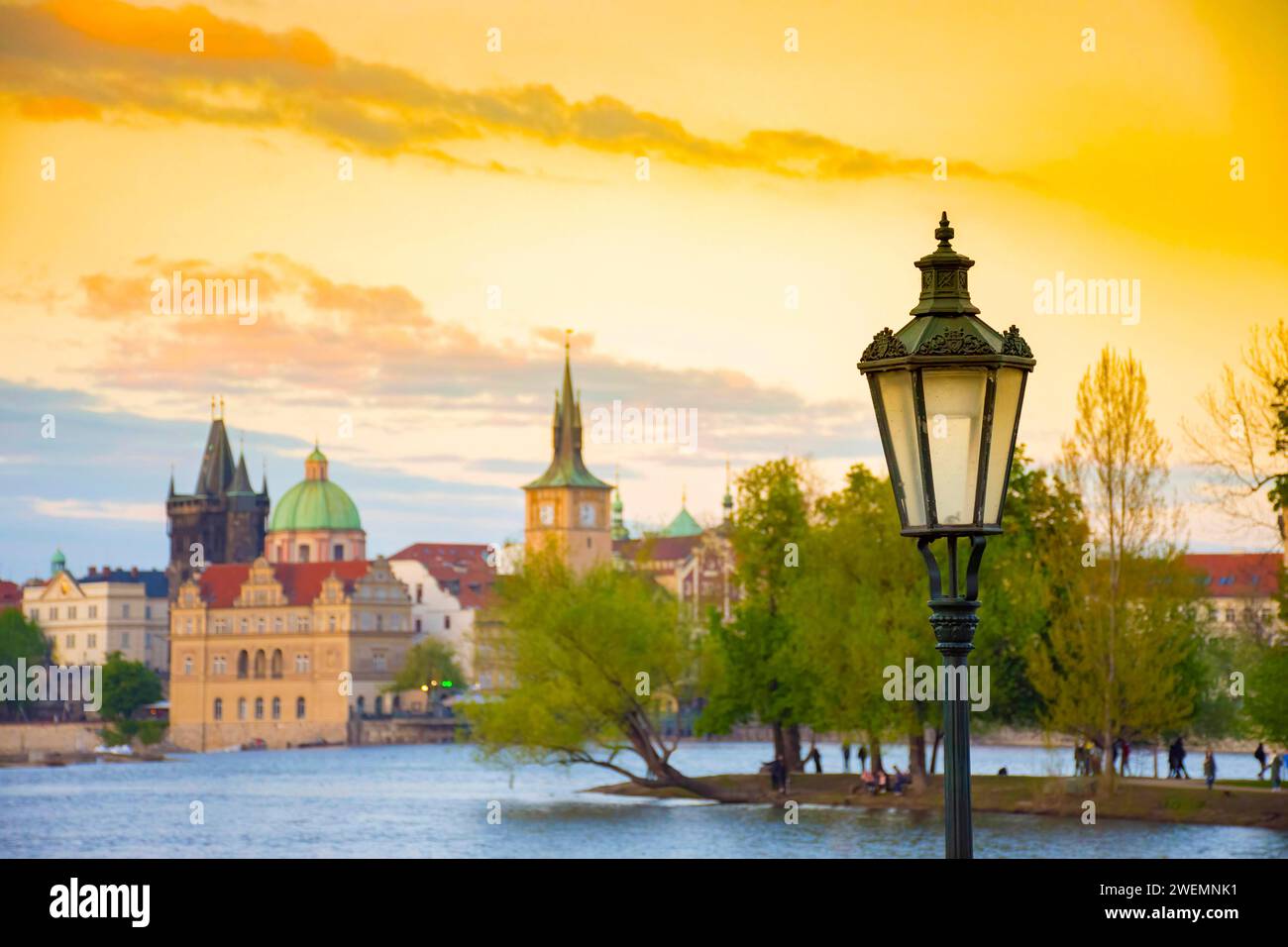 Vista offuscata dell'isola di Strelecky sul fiume Moldava e della città vecchia di Praga, Repubblica Ceca, al tramonto. Messa a fuoco selettiva sull'illuminazione stradale Foto Stock