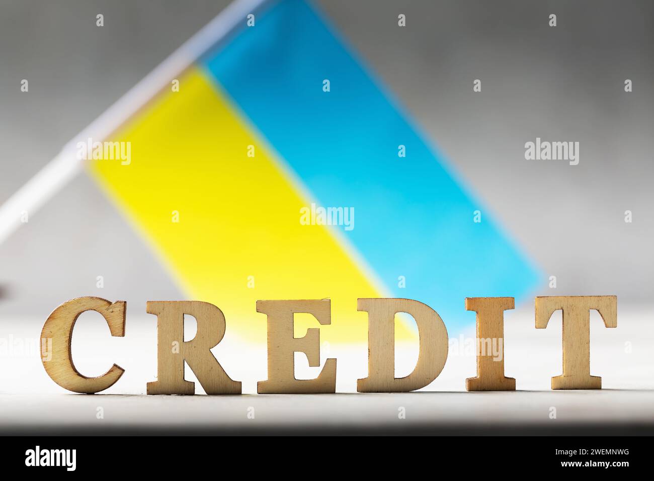 Testo con lettere di legno e bandiera Ucraina su sfondo astratto, concetto sul tema dell'onere del debito del popolo ucraino Foto Stock