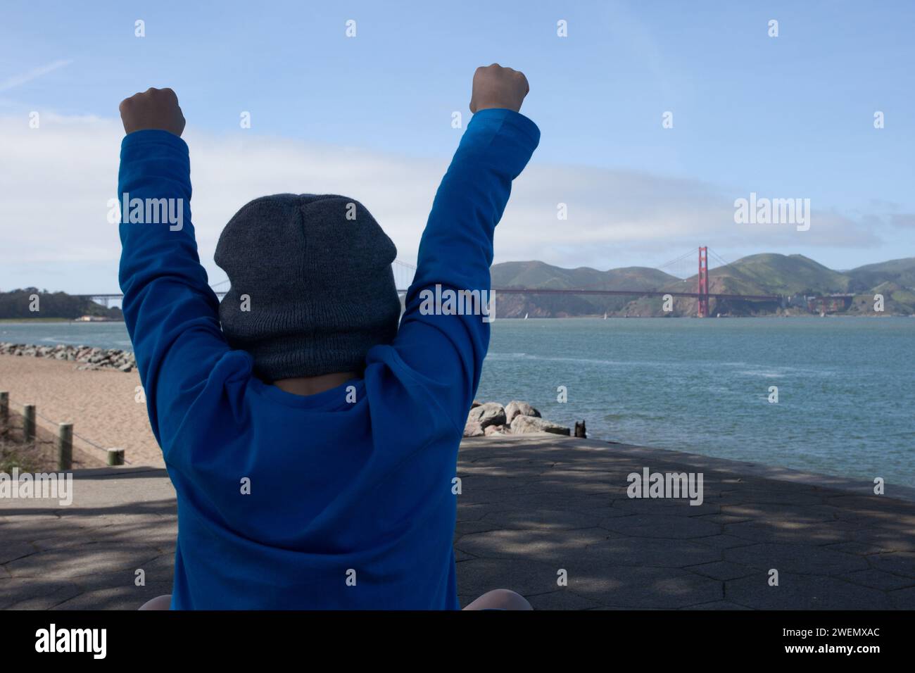Giovane ragazzo che tira al Golden Gate Bridge nella baia di San Francisco, con le braccia alzate per festeggiare, felice di vederlo. Foto Stock