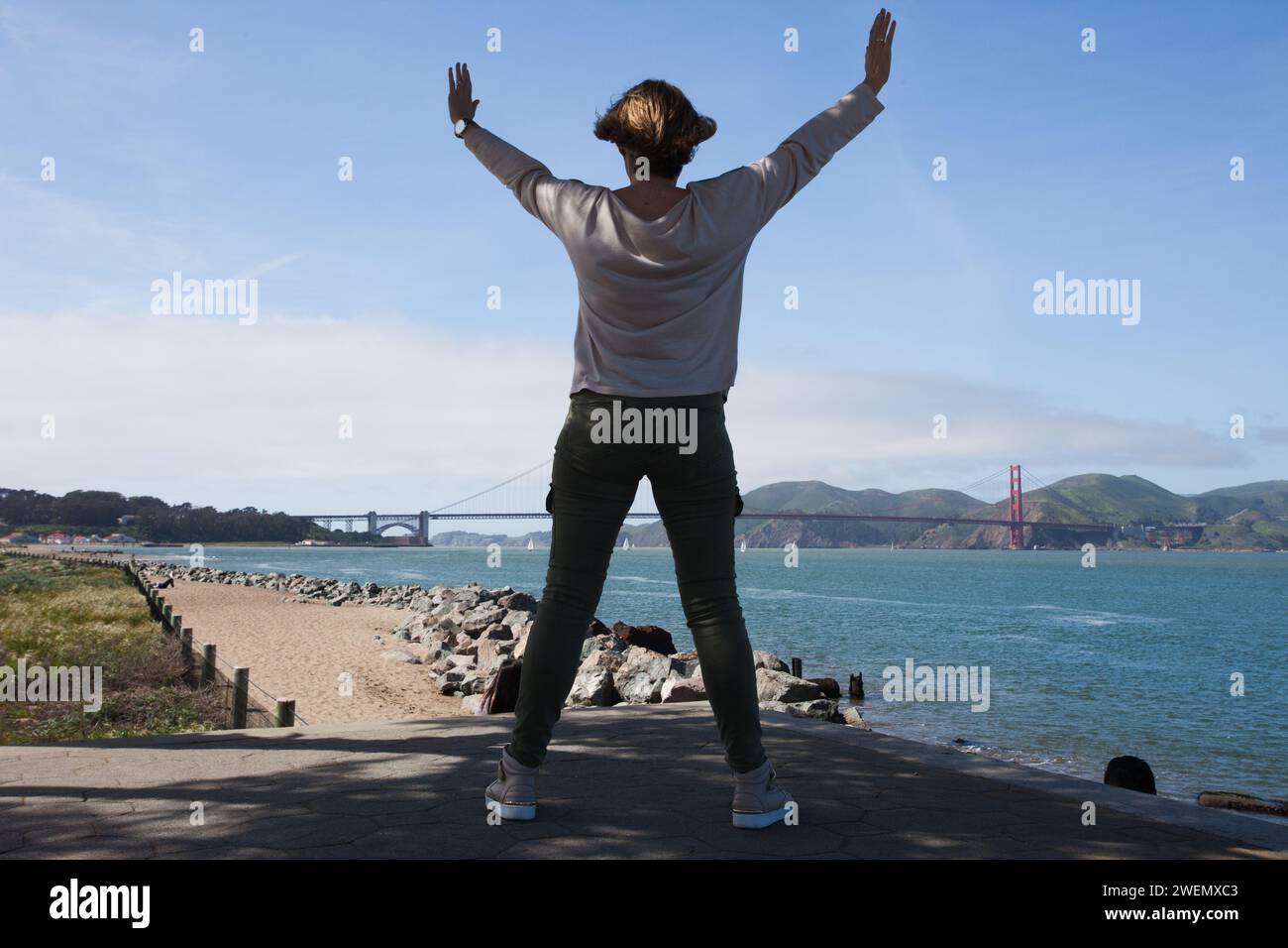 Giovane donna che guarda l'iconico Golden Gate Bridge che attraversa il Golden Gate di San Francisco, California, da un punto di osservazione. Foto Stock