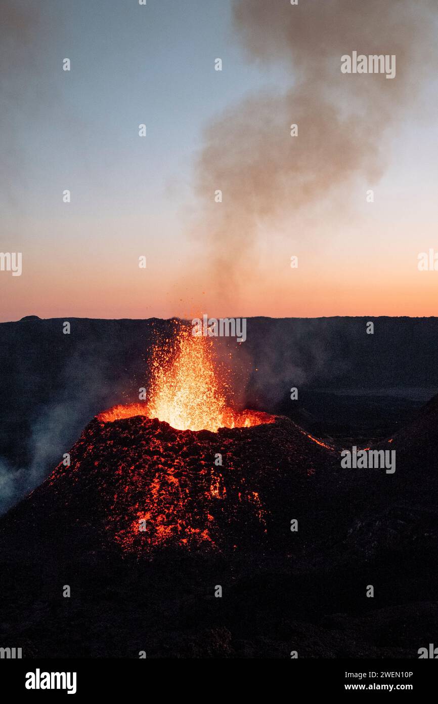 Una fotografia che cattura l'eruzione del vulcano Piton de la Fournaise mentre lancia lava sullo sfondo di un sole che tramonta. Foto Stock