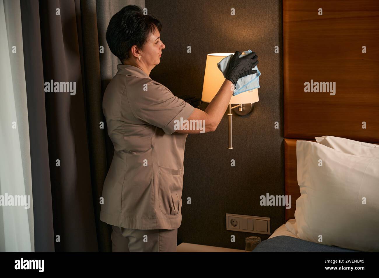 La cameriera con i guanti spolverava i mobili della suite Foto Stock