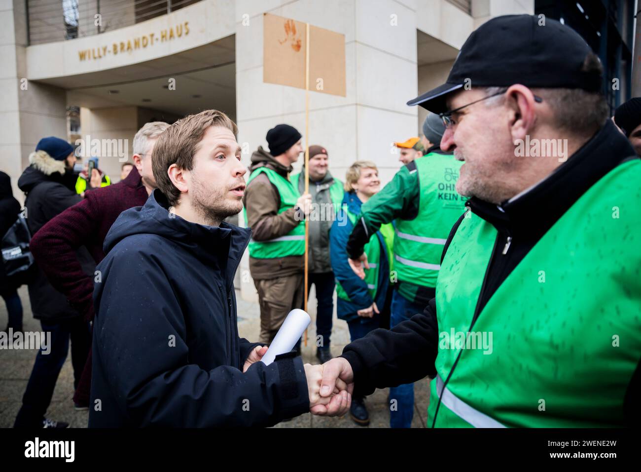 26 gennaio 2024, Berlino: Kevin Kühnert (l), segretario generale della SPD, e Henrik Wendorff, presidente della Brandeburgo State Farmers' Association, salutano durante una protesta con una sfilata di trattori organizzata dalla Brandenburg State Farmers' Association contro l'aumento della tassa sul gasolio agricolo di fronte alla Willy Brandt House (sede della SPD). Più di 300 agricoltori dello stato federale del Brandeburgo hanno guidato a Berlino da diverse direzioni il venerdì mattina. Con un totale di 250 trattori, hanno presentato venerdì davanti alla sede del partito del "semaforo" Foto Stock