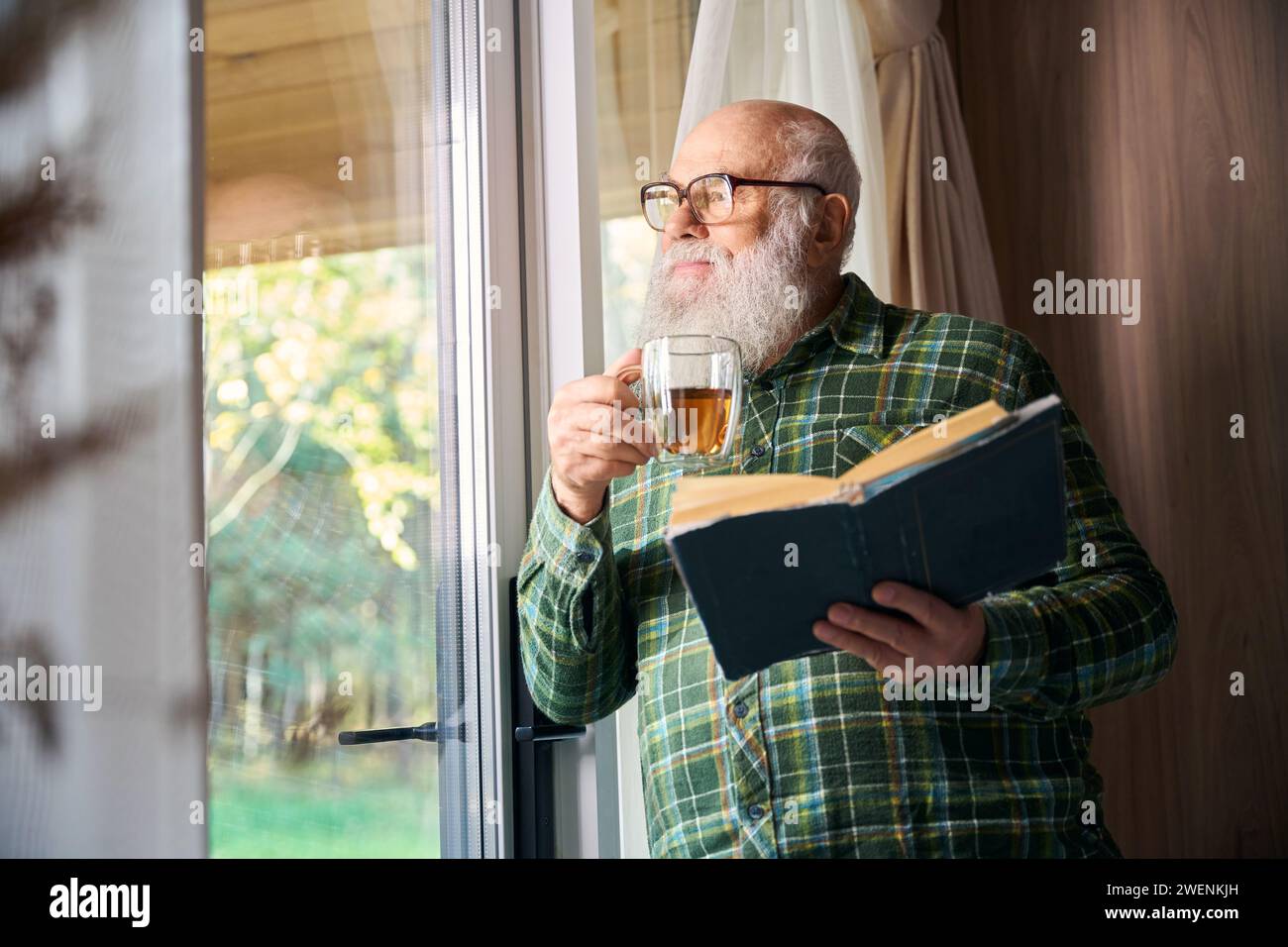L'uomo anziano si gode una tazza di tè vicino alla finestra Foto Stock