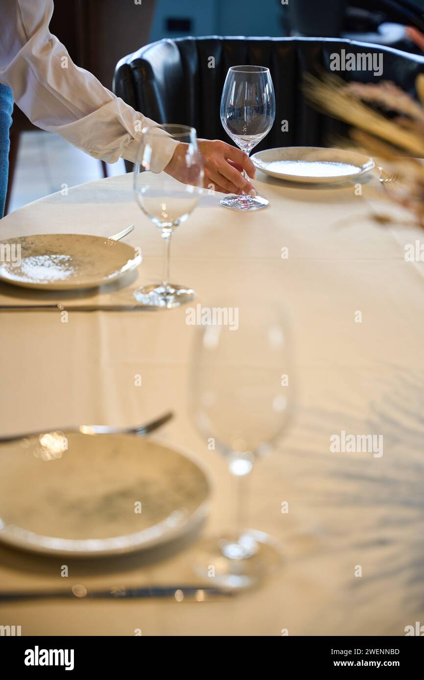 La cameriera con una giacca bianca serve un tavolo in una sala ristorante, c'è una tovaglia bianca sul tavolo Foto Stock