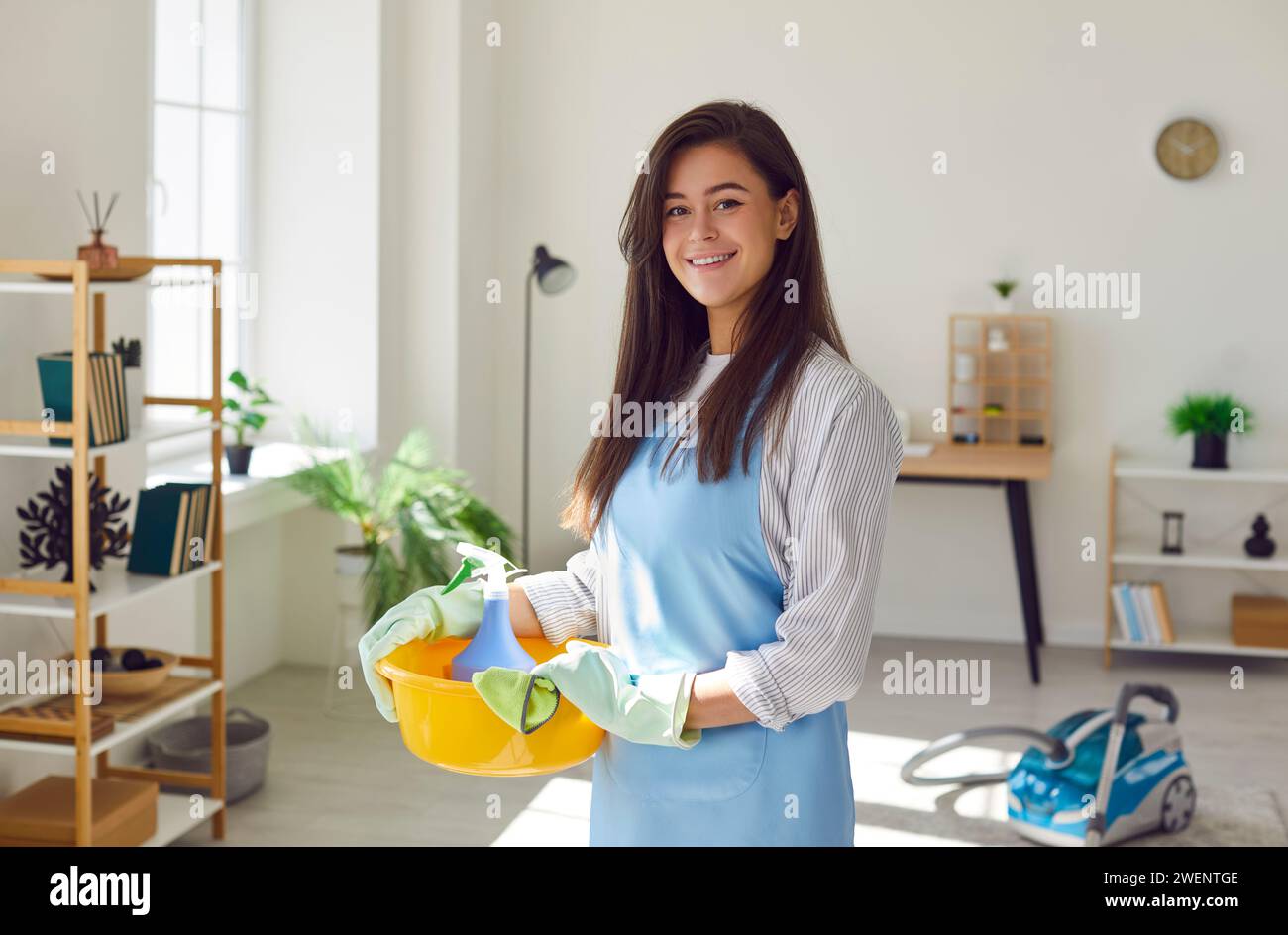 Donna casalinga con attrezzi e stracci per la pulizia, in salotto e guardando la macchina fotografica. Foto Stock