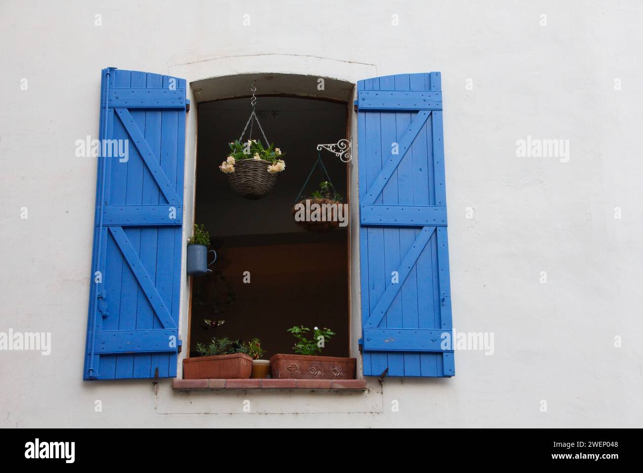Finestra aperta della casa francese del villaggio con persiane di legno blu e vasi di fiori appesi Foto Stock