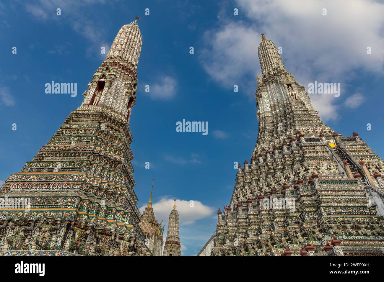 Due torreggianti prangs al Wat Arun (Tempio dell'Alba), a Bangkok, Thailandia. Altre prangs visibili sullo sfondo. Cielo blu e nuvole in alto. Foto Stock