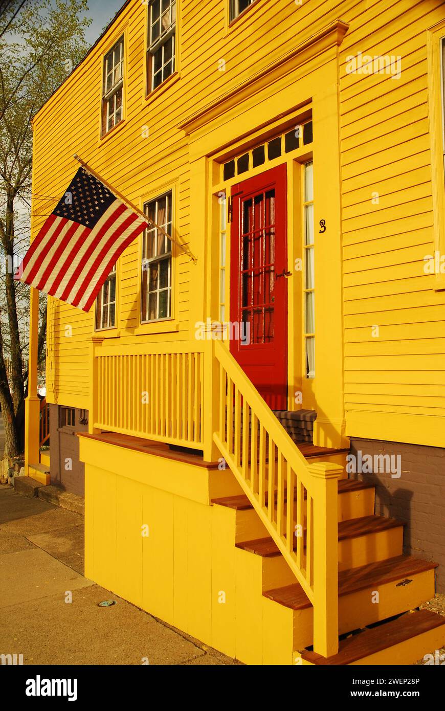 Una bandiera americana ondeggia di fronte a una casa gialla unica nella storica Newburyport, Massachusetts Foto Stock