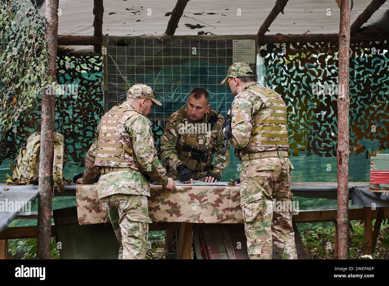 Un'unità militare altamente addestrata pianifica e organizza una missione tattica mentre studia una mappa militare durante una sessione informativa Foto Stock