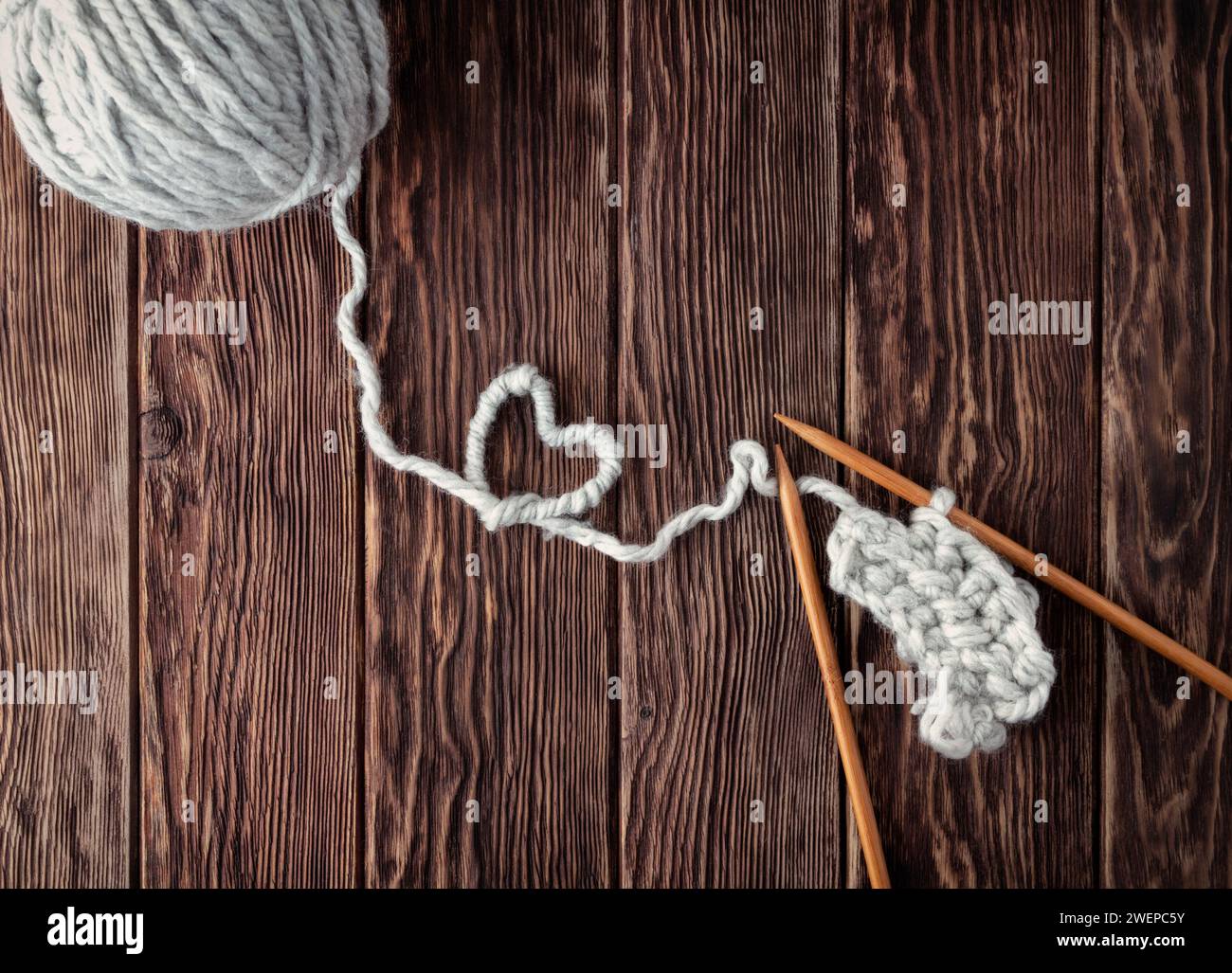Una sfera di filo e aghi per maglieria su uno sfondo di legno. Un cuore di filo come concetto di amore per il ricamo e la maglieria. Foto Stock