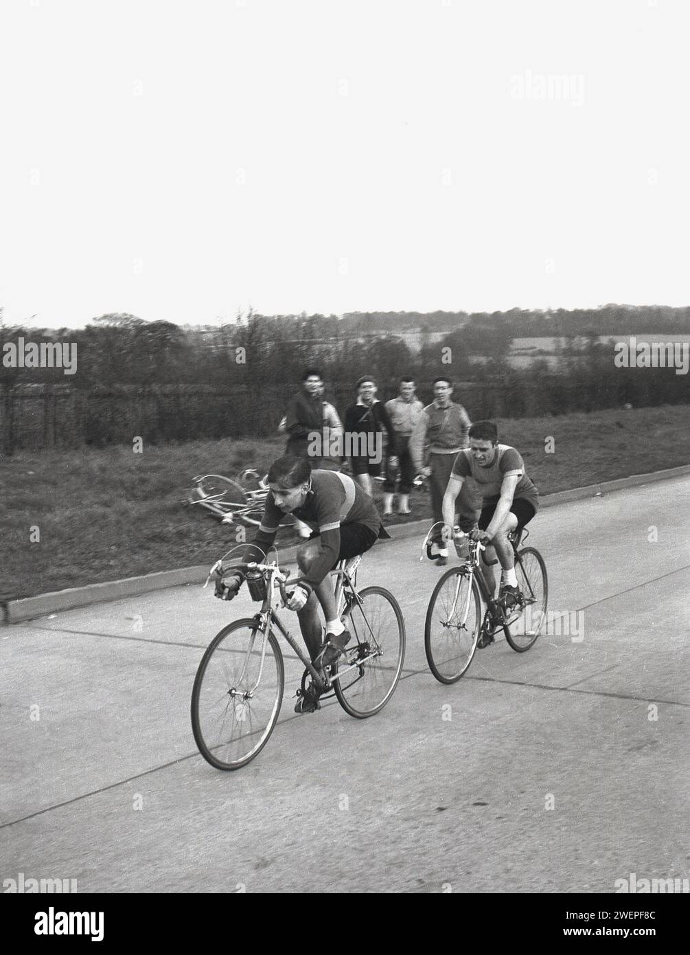 Anni '1960, storico, sport ciclistico, quattro spettatori maschili in piedi lungo la strada, guardando due ciclisti su strada, gareggiando nella corsa ciclistica amatoriale, il Daily Express Tour of Britain, Inghilterra, Regno Unito. Foto Stock
