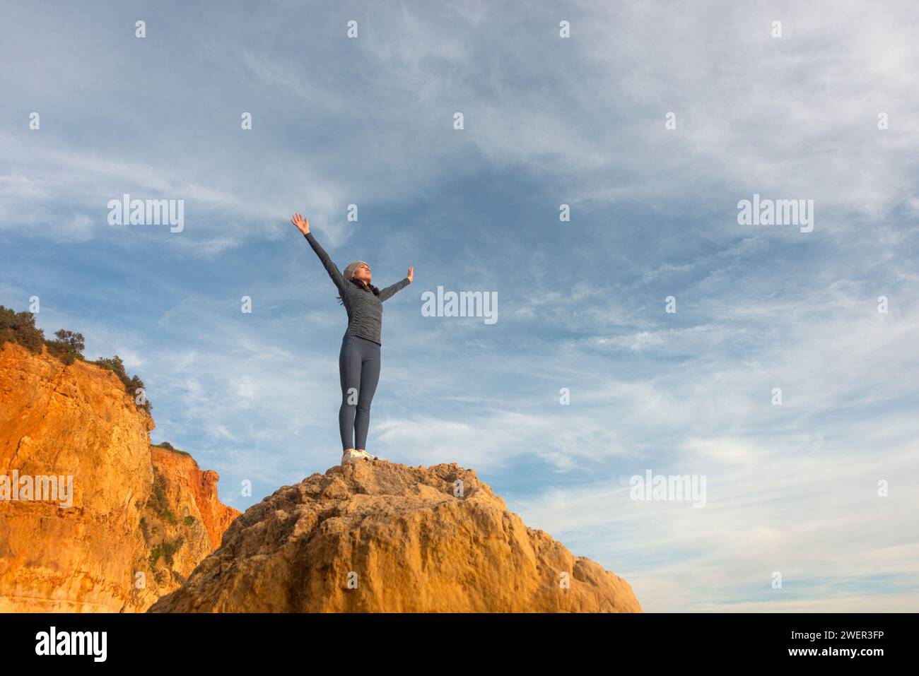 donna con le braccia alzate dopo aver scalato una roccia e in piedi sulla cima Foto Stock