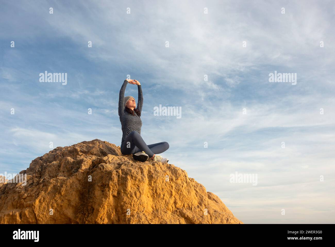 vesti una donna sportiva seduta sopra le braccia di una roccia, al di sopra dell'allungamento della testa Foto Stock