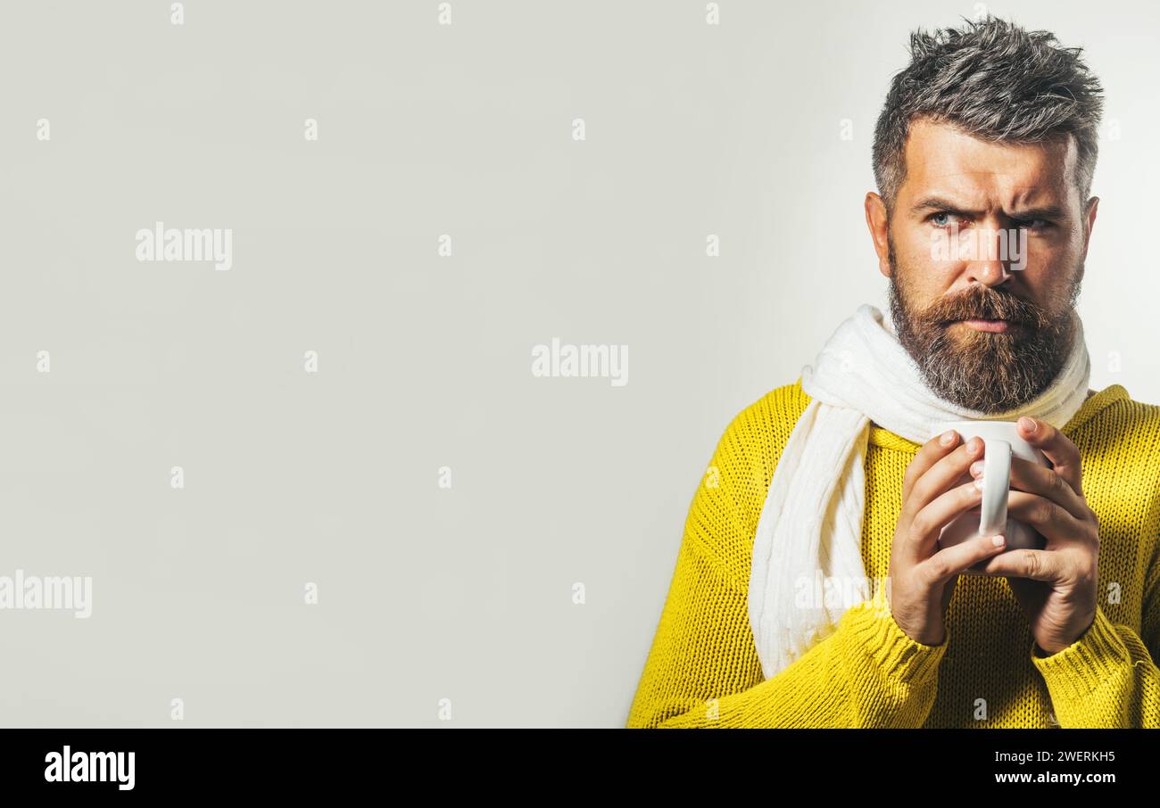 Uomo dalla barba seria con maglione a maglia e sciarpa con tazza di caffè caldo o tè. Autunno o inverno. Bel maschio in abiti caldi alla moda Foto Stock