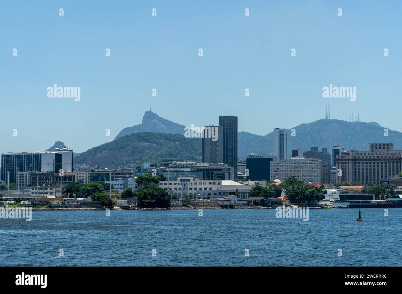 Edifici sul lungomare del quartiere Centro, come visto dalla baia di Guanabara acque blu con il monte Corcovado sul retro sotto il cielo azzurro del sole pomeridiano estivo. Foto Stock