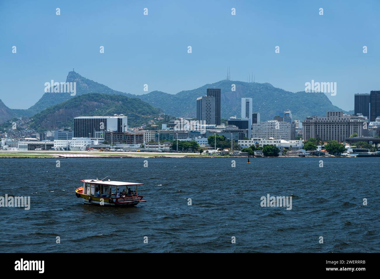 Edifici sul lungomare del quartiere Centro visti dalle acque blu della baia di Guanabara, vicino all'aeroporto Santos Dumont nel centro città sotto il cielo blu del pomeriggio estivo. Foto Stock